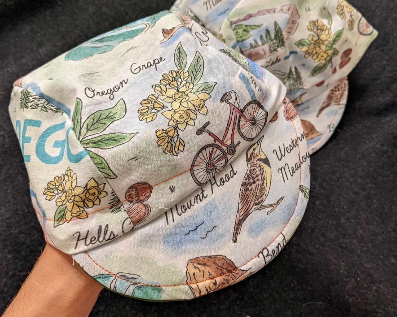 A pile of cycling caps made out of fabric with a bunch of Oregon landmarks on it.